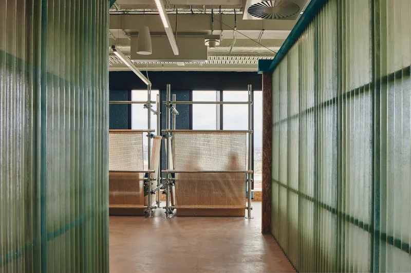 Corridor flanked by translucent corrugated panel partitions with green frames and exposed ceiling services