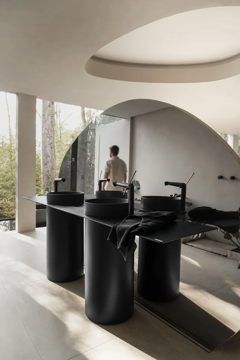 Bathroom with cylindrical black basins beneath a curved ceiling soffit and forest view