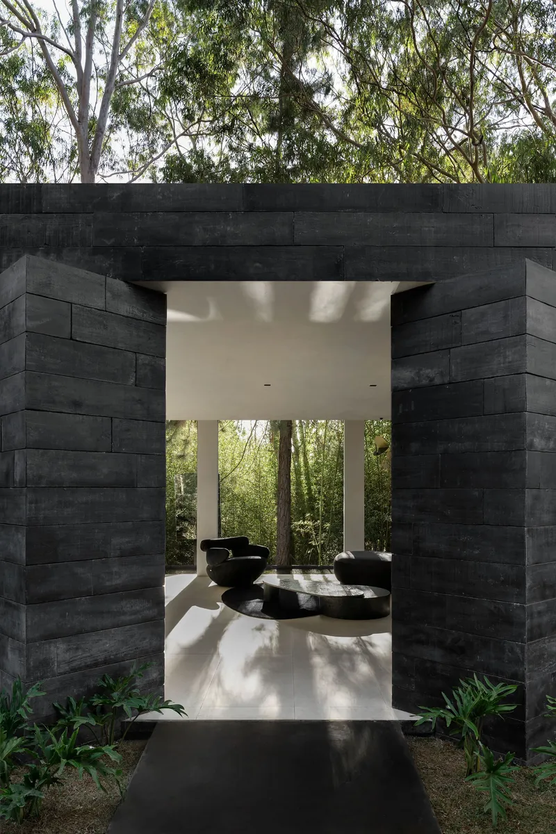 Frontal view of the blackened timber portal framing an interior courtyard with sculptural seating