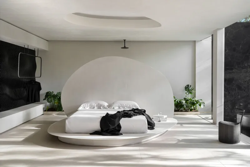 Bedroom with circular platform bed beneath arched ceiling recess and dappled sunlight from adjacent courtyard