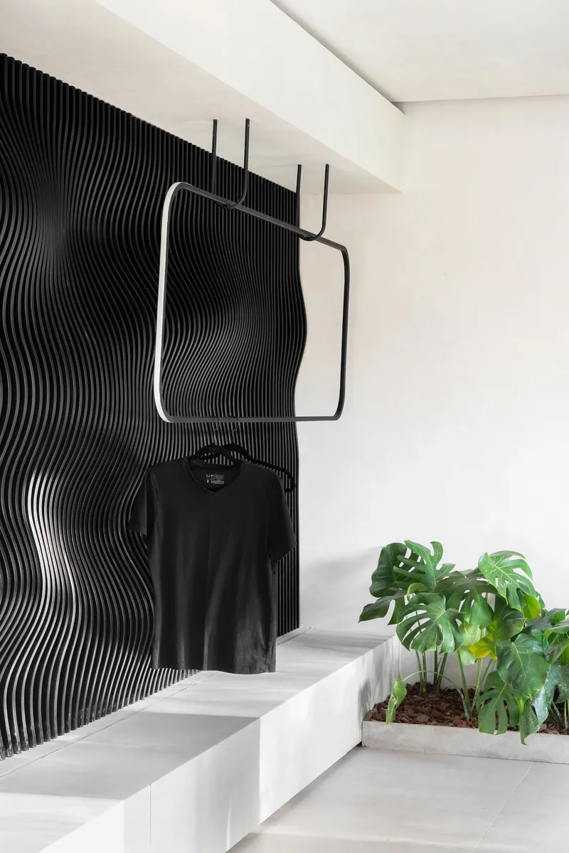 Black ribbed wall panel behind a steel clothing rack and white stepped seating with potted plants
