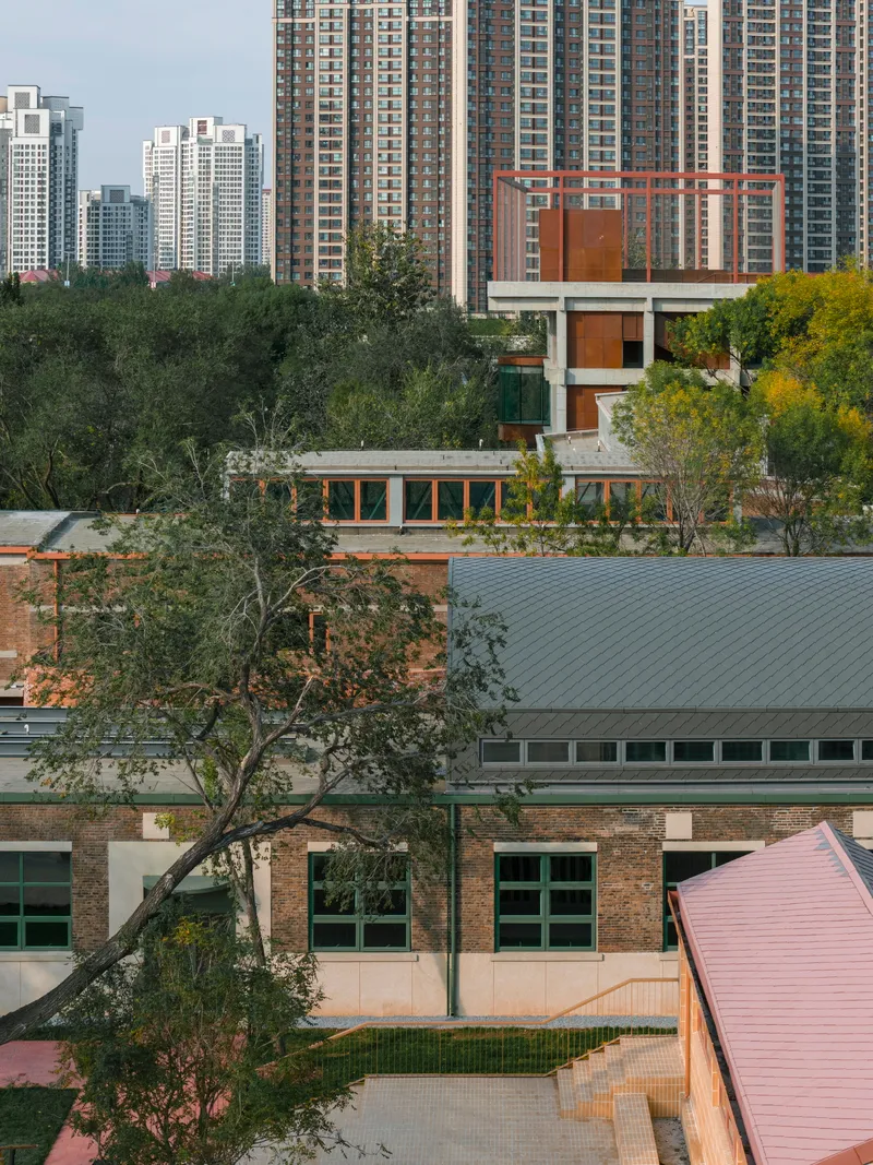 Elevated tower with rust-colored metal screens and glass walls emerging from treetops with apartment blocks behind