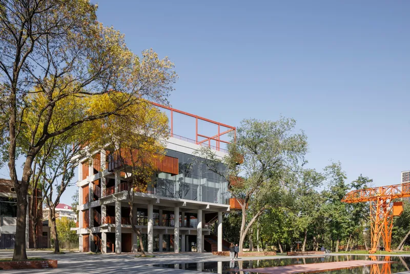 Corner facade showing concrete columns, glass walls, and weathered steel balconies framed by deciduous trees