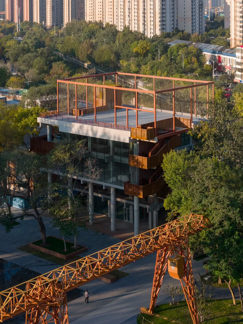 Aerial view of the rooftop terrace with red steel frame surrounded by park greenery and residential towers