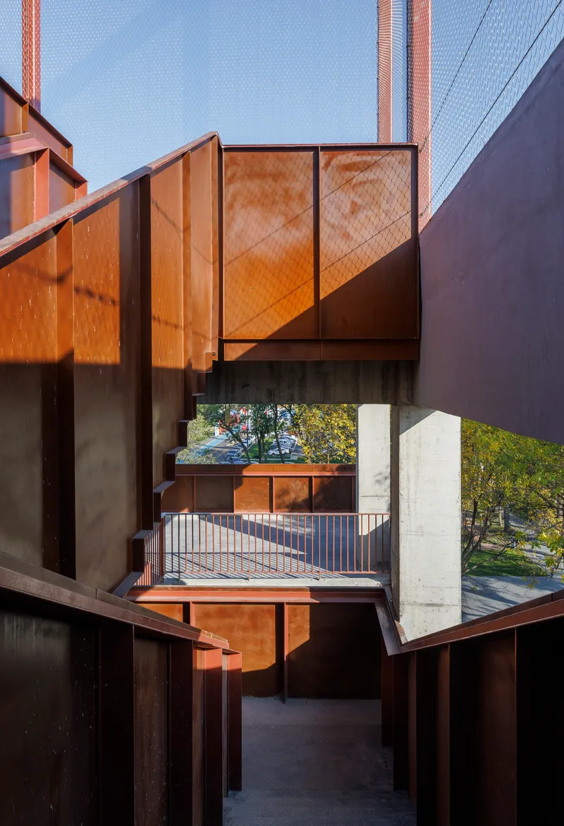 Framed view through stacked weathered steel balconies and concrete floor slabs at dusk