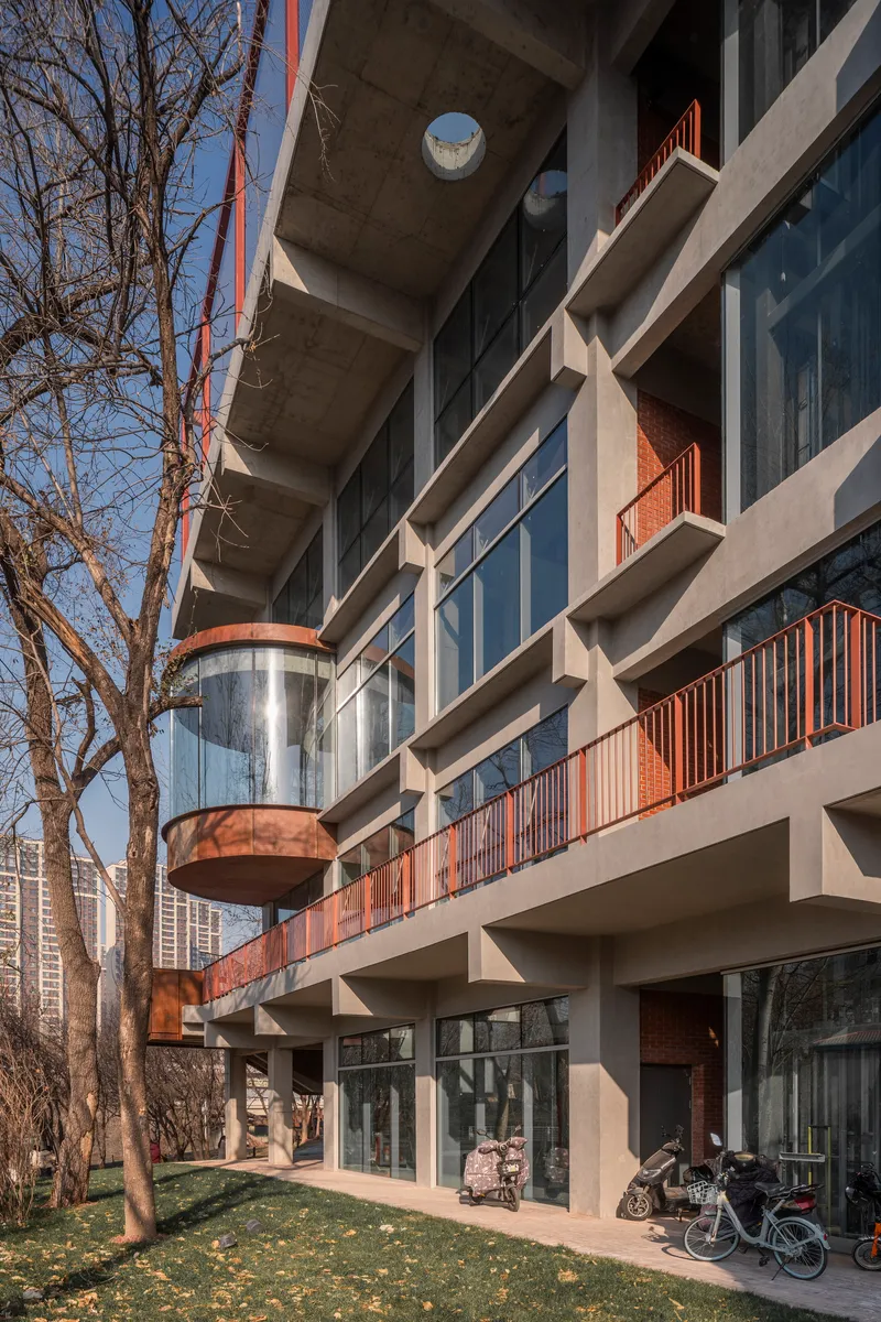 Facade detail showing concrete structure, glass elevator shaft, and corrugated metal balcony railings in afternoon light