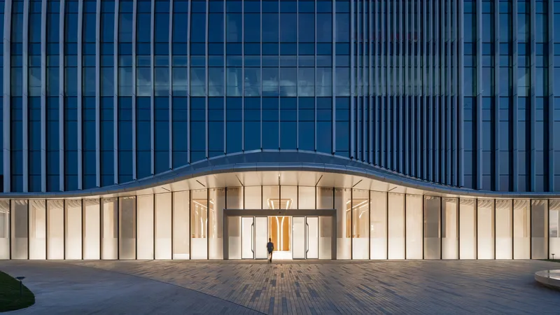 Street-level entrance with curved canopy and vertical stone panels beneath a glazed tower at dusk