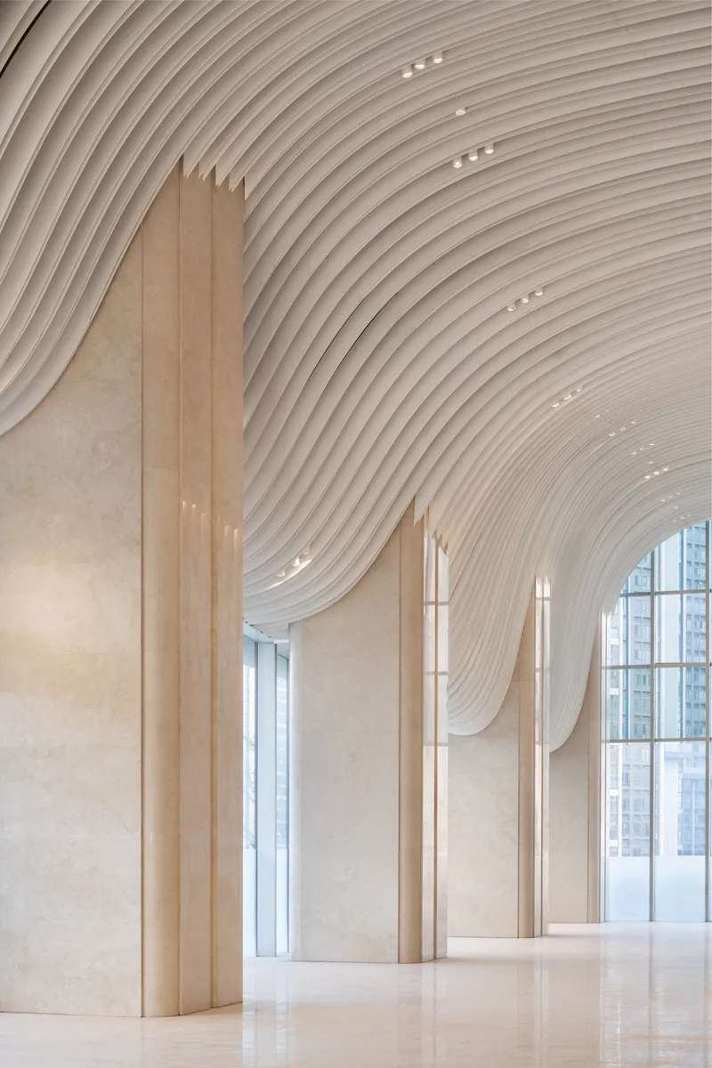 Close-up of stone column meeting the flowing ribbed ceiling with tall glazed curtain wall beyond