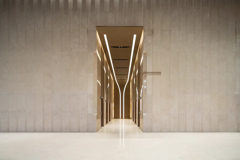 Elevator lobby framed by illuminated vertical mullions and polished stone floor reflecting overhead lighting
