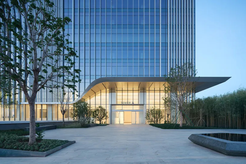 Glass tower base with curved canopy entrance flanked by trees and reflecting pool at dusk