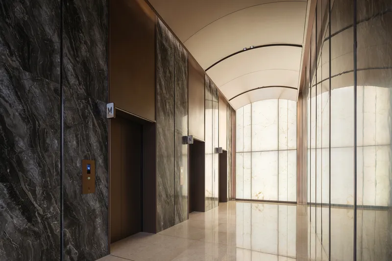 Elevator lobby with dark veined stone walls and arched translucent glass partition under barrel vault ceiling