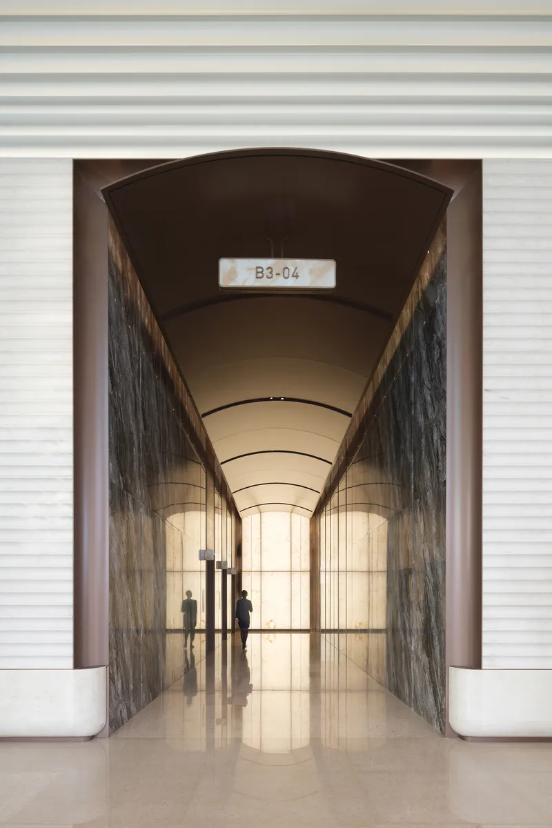 Arched passageway with barrel vault ceiling and veined stone walls framing silhouettes in polished floor reflection