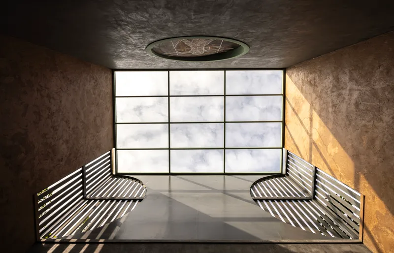 Rooftop terrace with slatted metal benches facing a gridded glass wall and circular skylight
