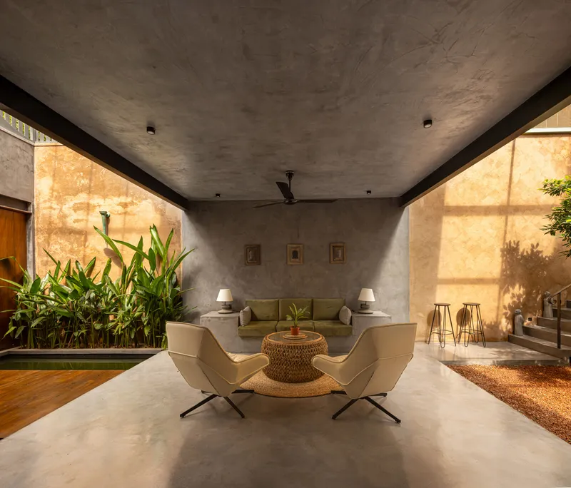 Living area with concrete ceiling and walls where afternoon sun casts shadows through adjacent plants