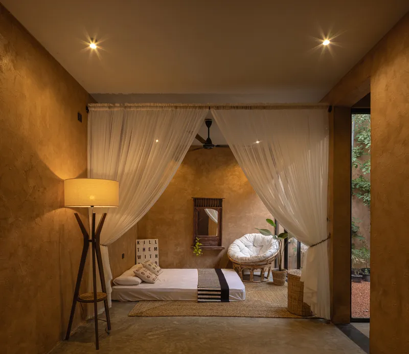 Bedroom framed by sheer white curtains with view to exterior courtyard at dusk