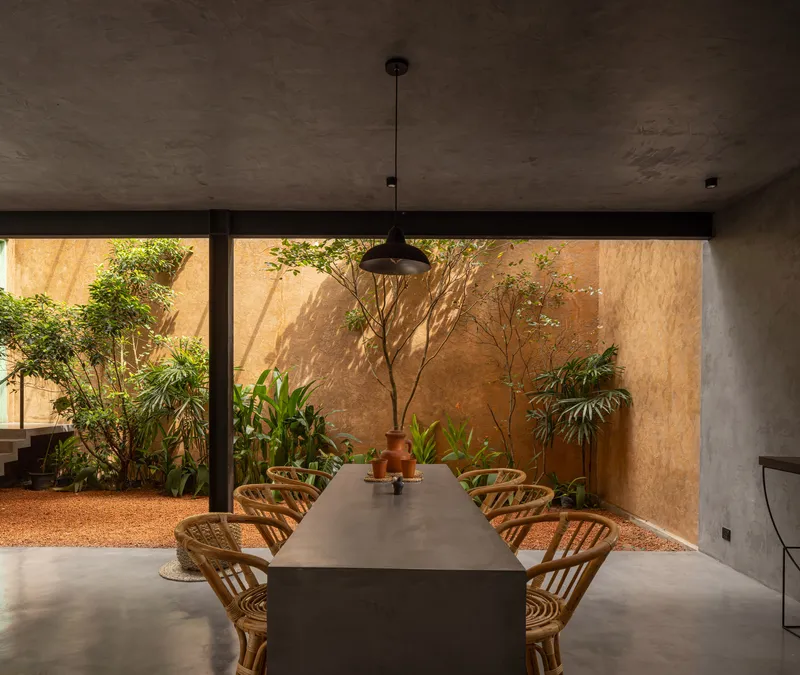 Dining space opening through frameless glass to courtyard with ochre walls and planted beds