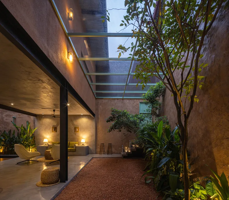 Interior courtyard with glass skylight overhead, planted tree and gravel floor at dusk