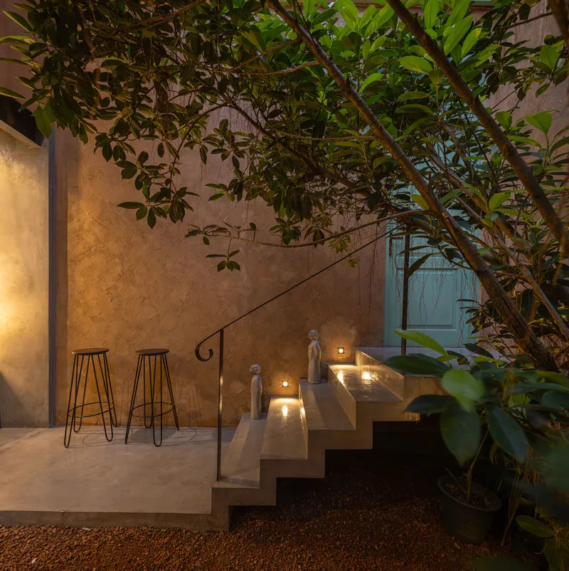 Stone staircase with wire-frame stools beside a planted tree at twilight