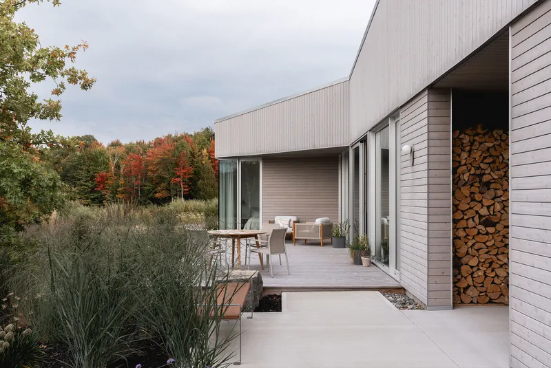 Concrete terrace with stacked firewood storage niche beside sliding glass doors and planted beds