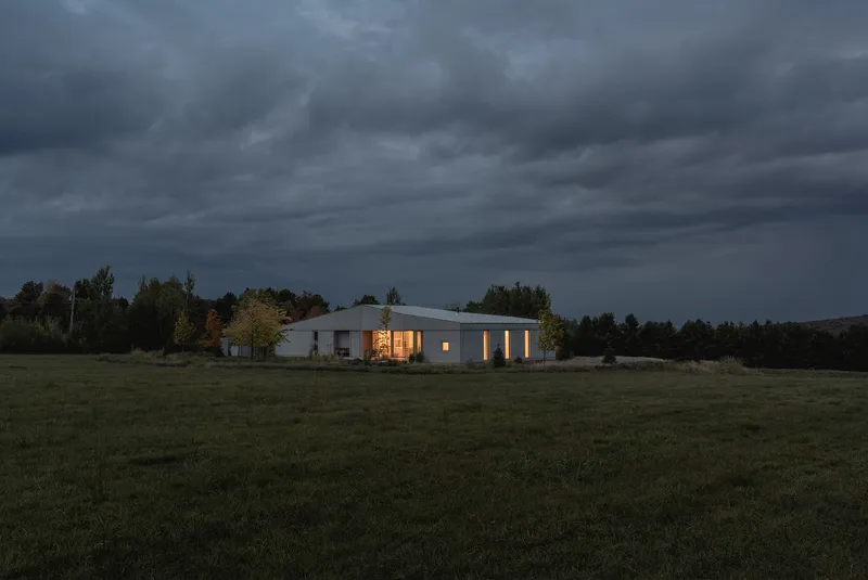 Night view of the illuminated residence across a dark meadow under heavy storm clouds
