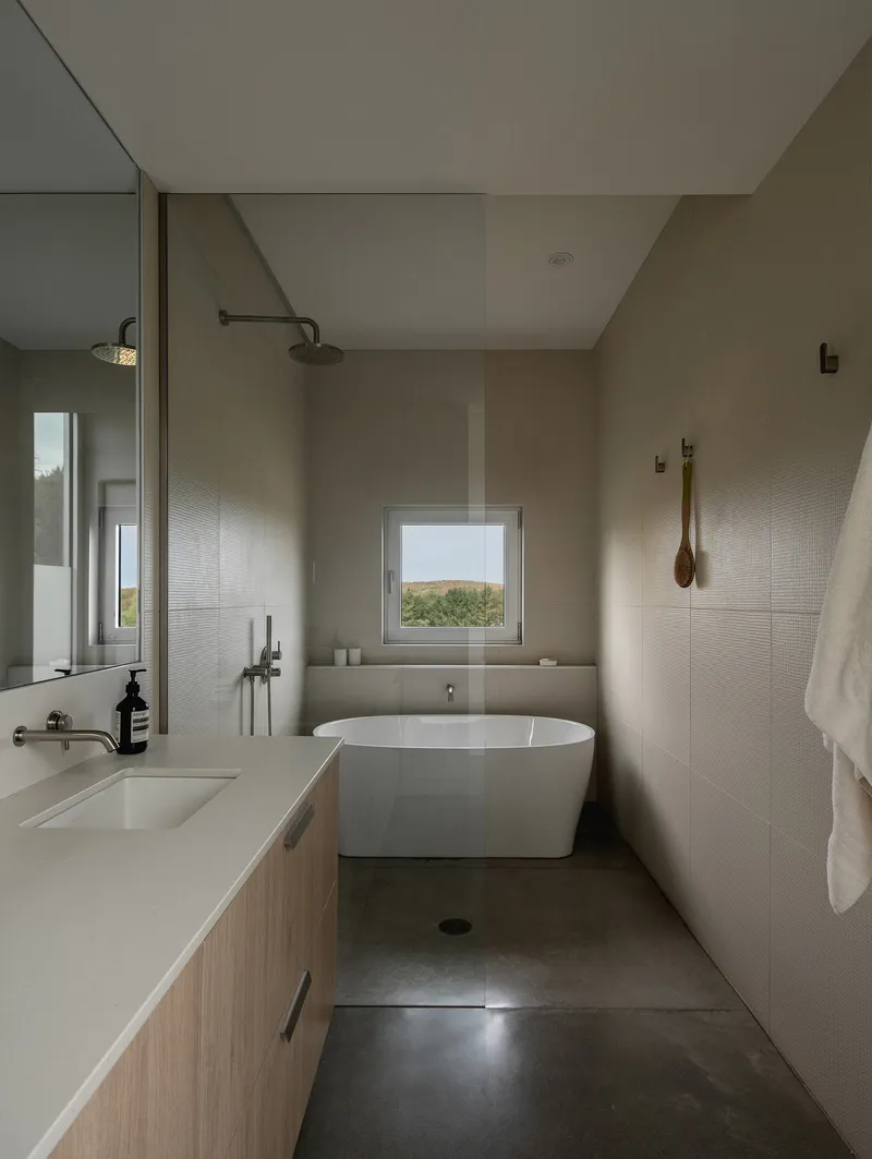 Bathroom with freestanding tub and glass shower enclosure framed by pale tile and a landscape window