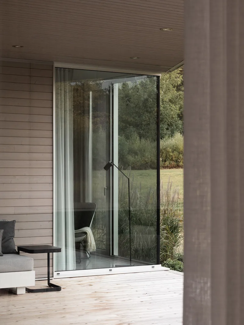 Open sliding glass door connecting timber deck to interior and overlooking grassy meadow with trees