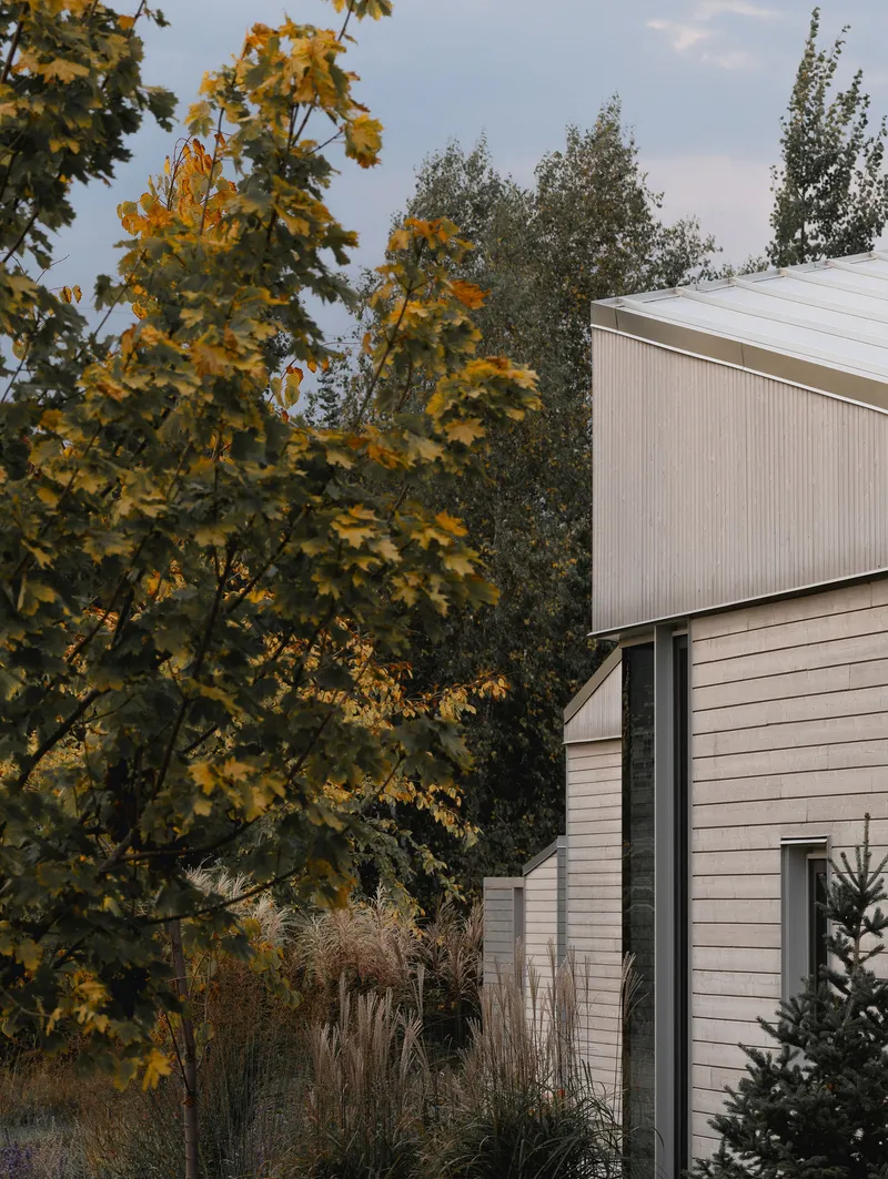 Exterior view of the ribbed metal upper volume rising above horizontal siding amid autumn foliage