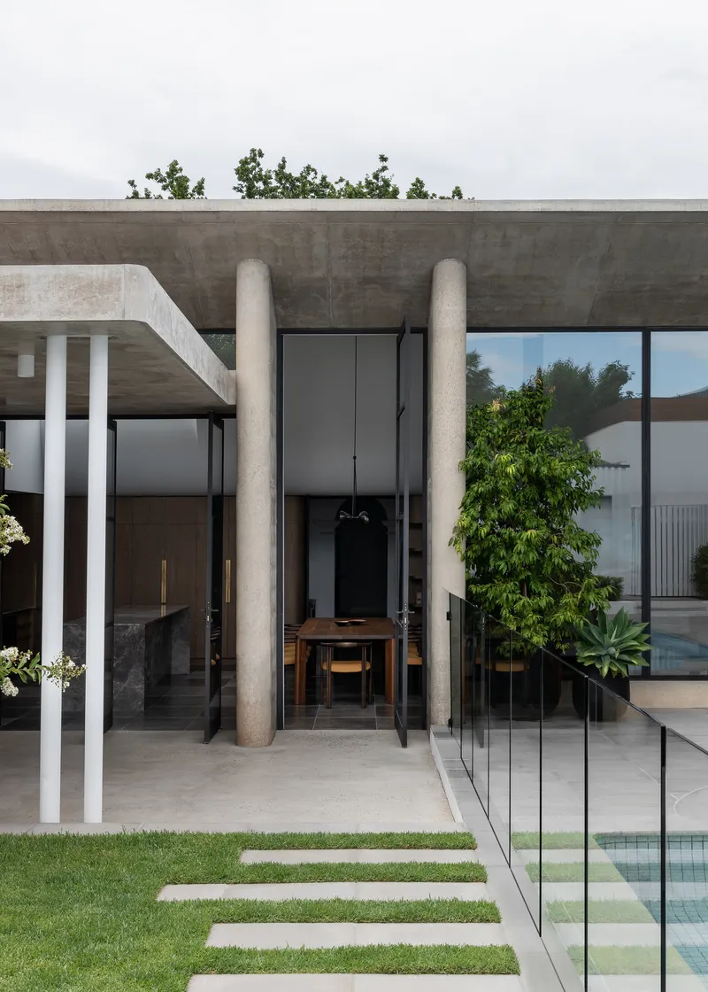 Entrance portico framed by concrete columns with glass balustrade and lawn stepping stones in foreground