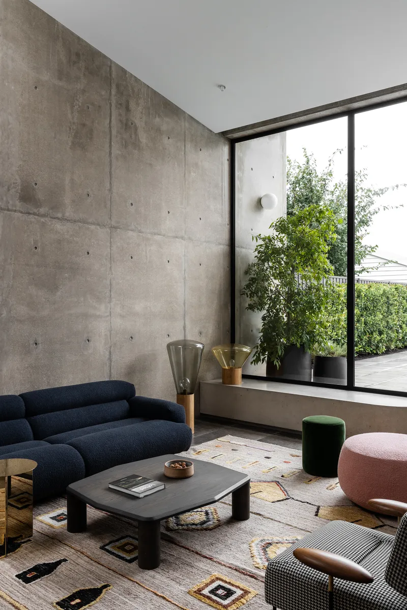 Corner seating area with board-formed concrete wall and floor-to-ceiling window overlooking planted terrace