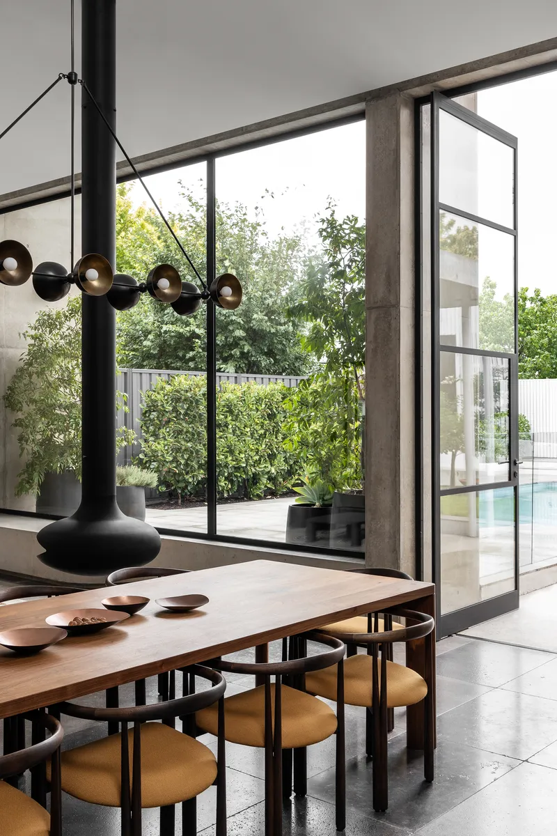 Dining area with steel-framed glass doors opening to a garden courtyard with dense plantings