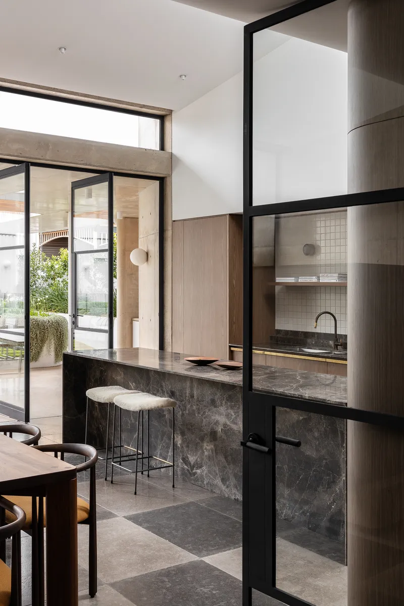View through steel-framed glass partition to kitchen with stone island and garden beyond