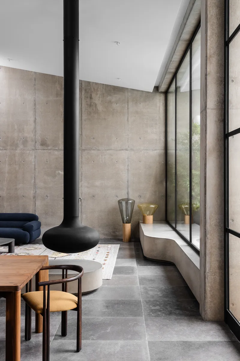 Double-height living space with board-formed concrete walls and floor-to-ceiling steel-framed glazing along one side