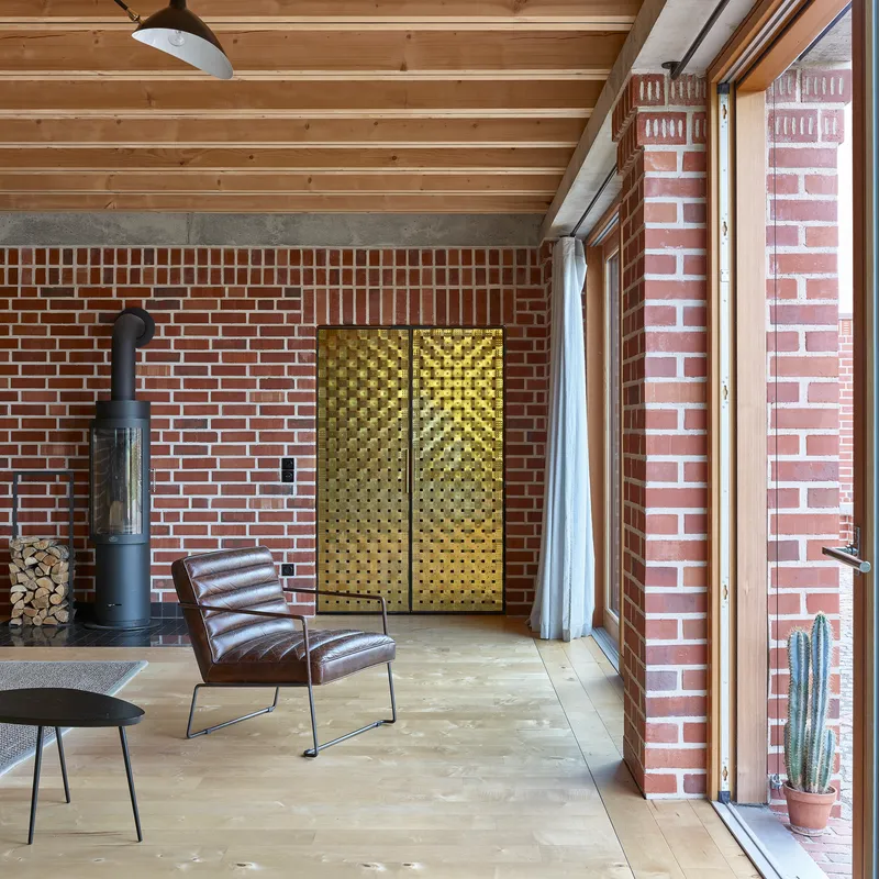 Interior living space with exposed timber ceiling, red brick walls, brass textured panels and leather chair