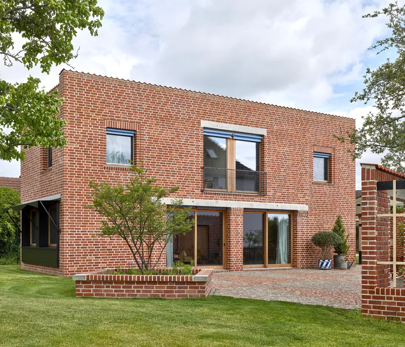 Two-story brick facade with timber-framed windows and low brick planter wall in lawn setting
