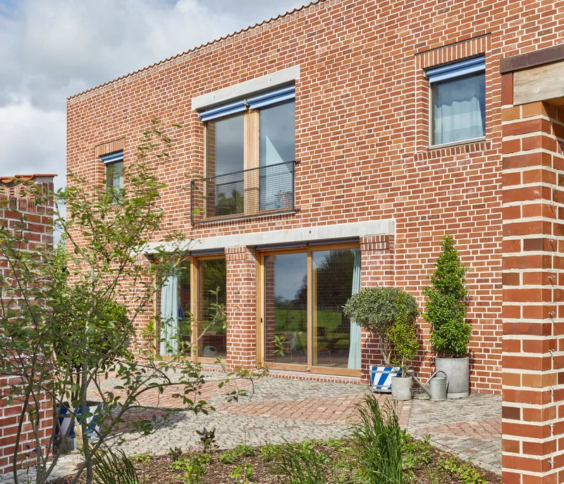Brick facade detail with paved courtyard terrace and small trees flanking glazed openings