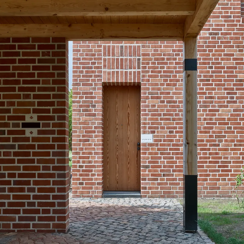 Timber entry door recessed in brick wall with exposed wood rafters overhead and cobblestone paving