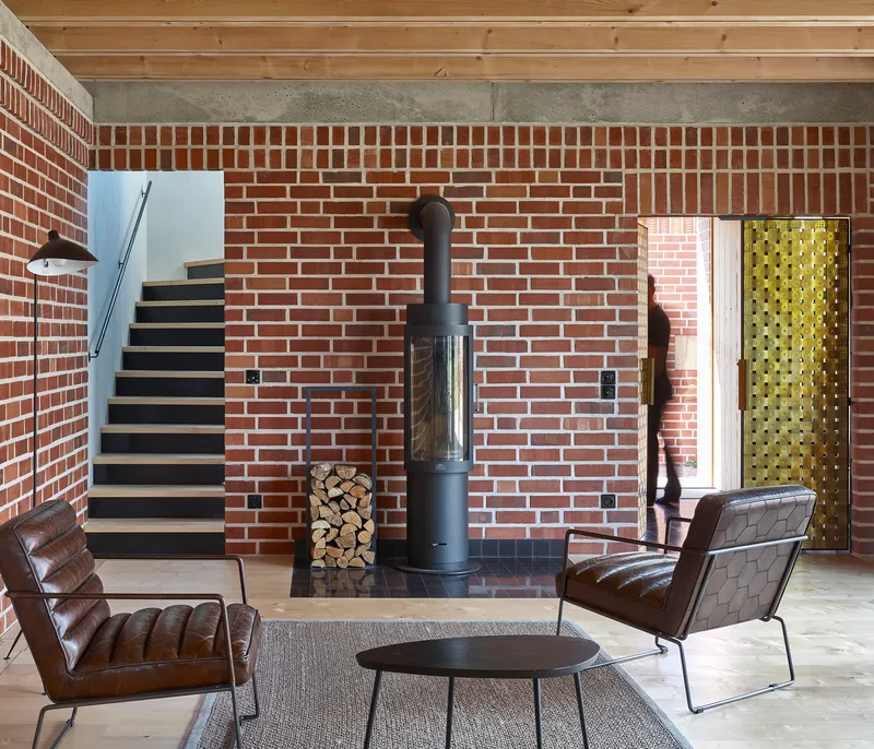 Interior living space with exposed brick wall, freestanding wood stove and floating timber staircase