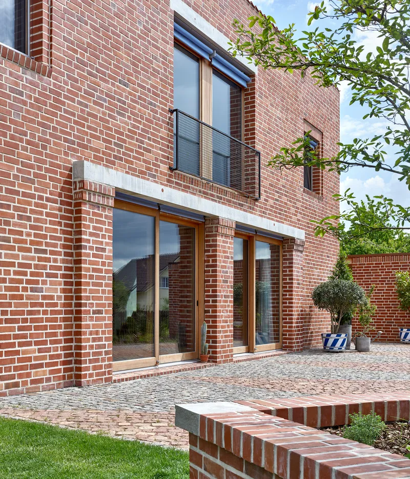 Rear courtyard elevation with sliding glass doors and upper balcony framed by brick walls and topiary