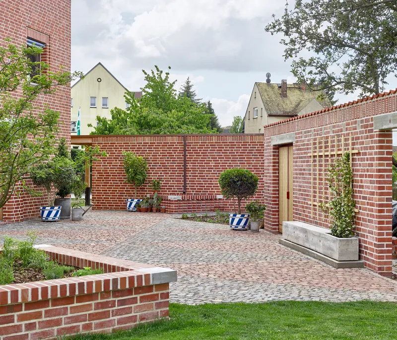 Enclosed brick courtyard with cobblestone paving and concrete planters beneath neighboring gabled roofs