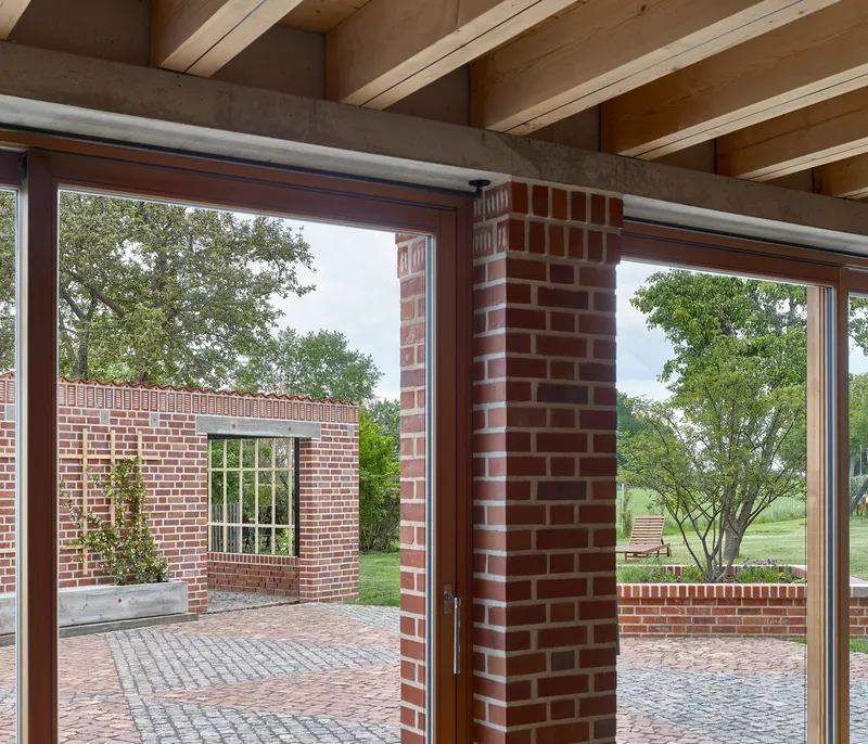 Interior view through glazed corner opening showing exposed timber joists and brick columns framing the courtyard