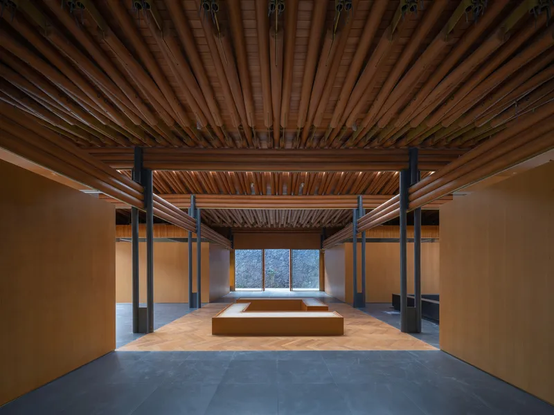 Gallery interior with radial timber ceiling panels and black steel columns framing a distant window