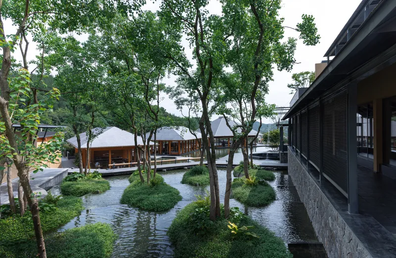 Water courtyard with planted islands, mature trees, and covered walkways under overcast sky