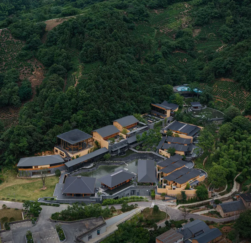 Aerial view of clustered pavilions with dark roofs surrounded by terraced hillsides and forest at dusk