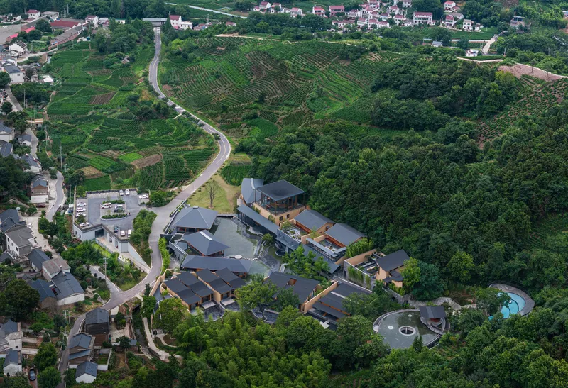 Drone view of the compound nestled between agricultural terraces and wooded slopes in daylight