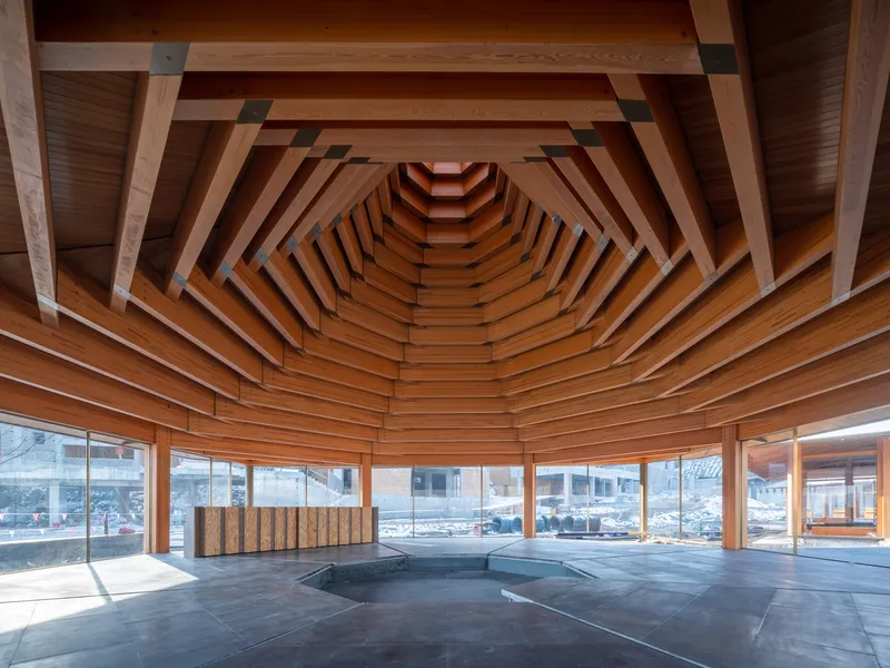 Laminated timber ceiling converging in concentric ribs above a dark tile floor with winter sunlight streaming in