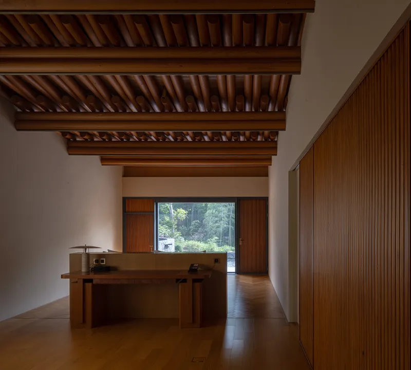 Interior view showing exposed timber ceiling beams and vertical wood slat wall with a horizontal window framing greenery