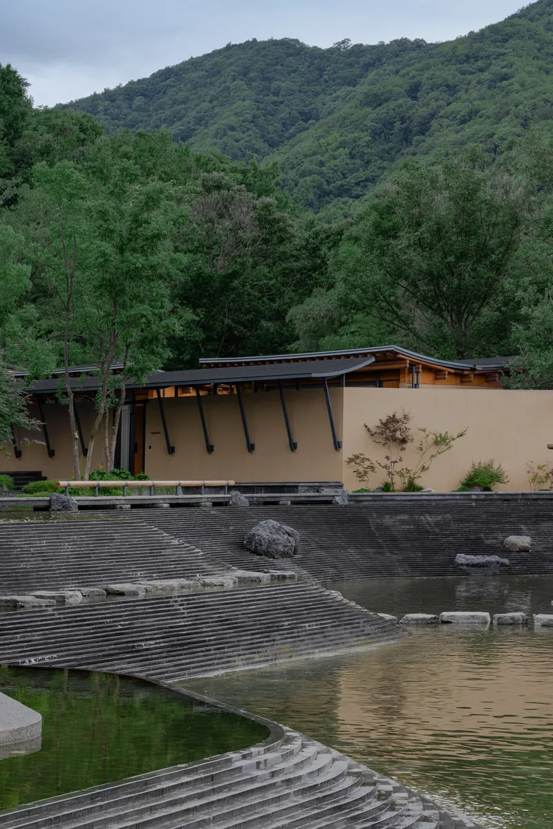 Exterior showing angled steel columns supporting a low-pitched roof beside a stepped stone water feature and reflecting pool
