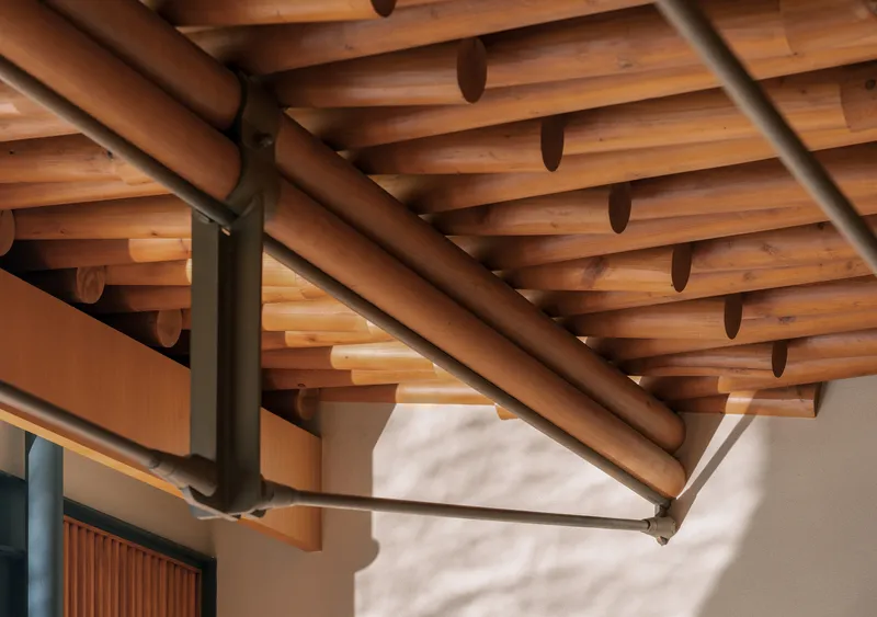 Detail of timber beams and steel brackets meeting a white stucco wall in afternoon light