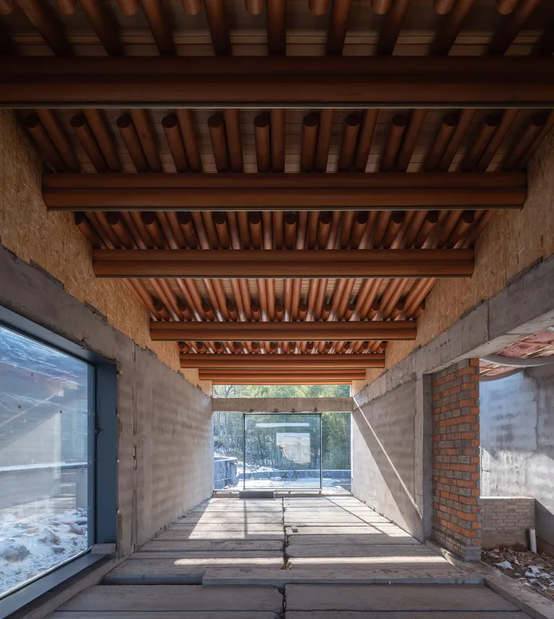Corridor with layered timber ceiling beams above concrete walls and wood plank flooring