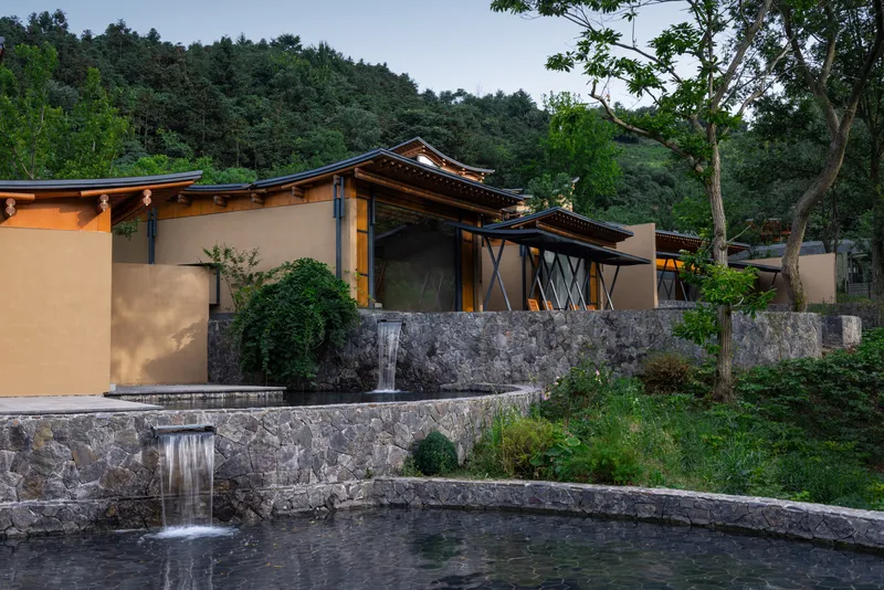 View of the residence on terraced stone retaining walls with water feature and forested hillside beyond
